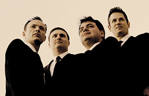 Jerusalem Quartet members grouped closely together wearing black suits looking above the camera placed at a downward angle