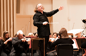 St. Louis Symphony Orchestra Music Director Stéphane Denéve standing in center of musicians with left arm out