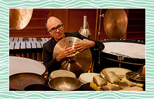 Steven Schick holding a cymbal while looking at the camera. 